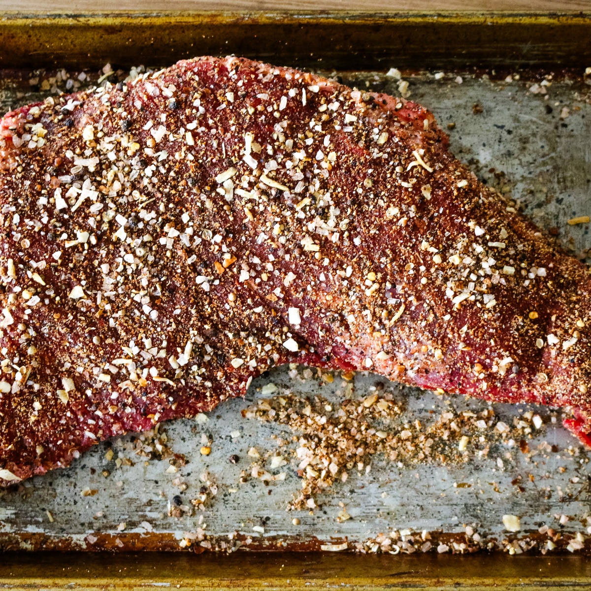 raw steak covered in seasonings on metal pan.