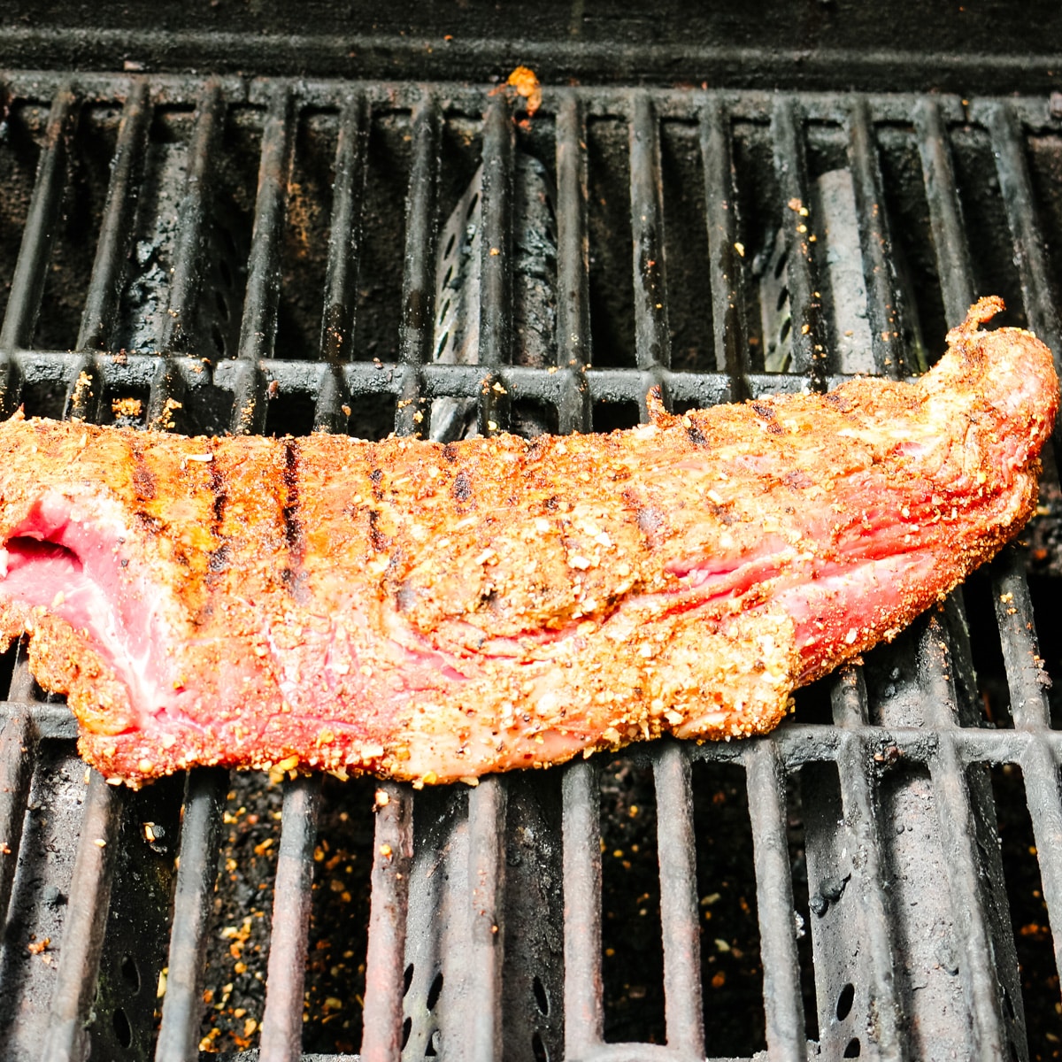 raw seasoned steak on a grill getting cooked.
