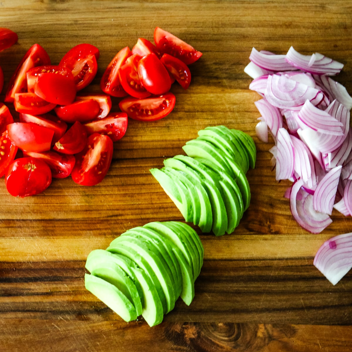 sliced avacados, tomatoes, and onion on a wooden cutting board.